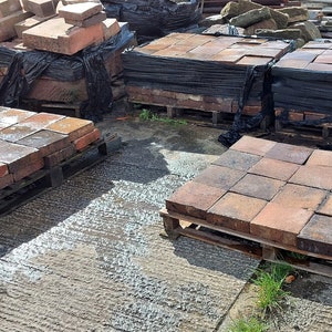 May include: Four pallets of red clay bricks, stacked and ready for use in a building project. The bricks are arranged in a grid pattern on the pallets.