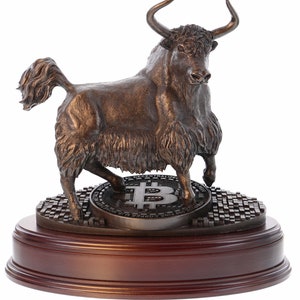 May include: A bronze sculpture of a yak standing on a round base with a Bitcoin coin. The yak is facing to the right and has a long, flowing tail. The base is made of wood and has a dark brown finish.