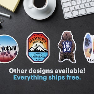 Peut inclure: Plusieurs autocollants sur le th&egrave;me de la Californie. Les motifs comprennent une sc&egrave;ne de coucher de soleil avec des palmiers, un logo de Mammoth Mountain, un ours tenant une pancarte avec "Cali for Nia" et des planches de surf. Le texte "Other designs available!" est &eacute;galement visible.
