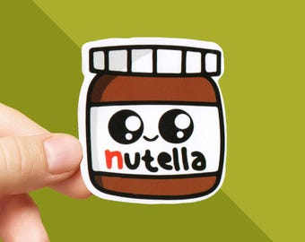 May include: A sticker featuring a cartoon illustration of a Nutella jar with large, expressive eyes. The jar is brown with a white label and the word "nutella" in black and red. The sticker is held against a green background.