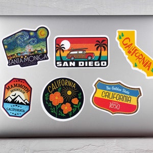 May include: A collection of colorful California-themed stickers on a laptop. Designs include Santa Monica, San Diego, Mammoth Mountain, and the state outline, featuring vibrant illustrations and text.