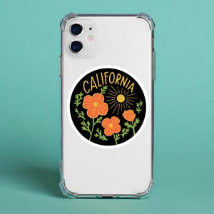Peut inclure: Un autocollant rond avec un fond noir, portant l'inscription "CALIFORNIA" en jaune. Le motif comprend des coquelicots orange, des feuilles vertes et un soleil jaune. L'autocollant est sur une coque de t&eacute;l&eacute;phone transparente.
