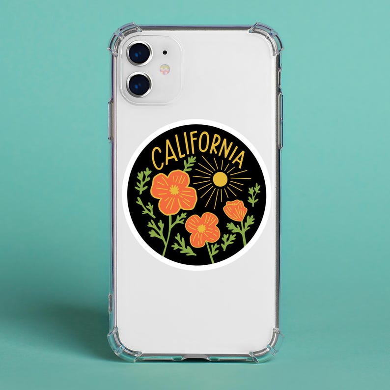 Peut inclure: Un autocollant rond avec un fond noir, portant l'inscription "CALIFORNIA" en jaune. Le motif comprend des coquelicots orange, des feuilles vertes et un soleil jaune. L'autocollant est sur une coque de t&eacute;l&eacute;phone transparente.