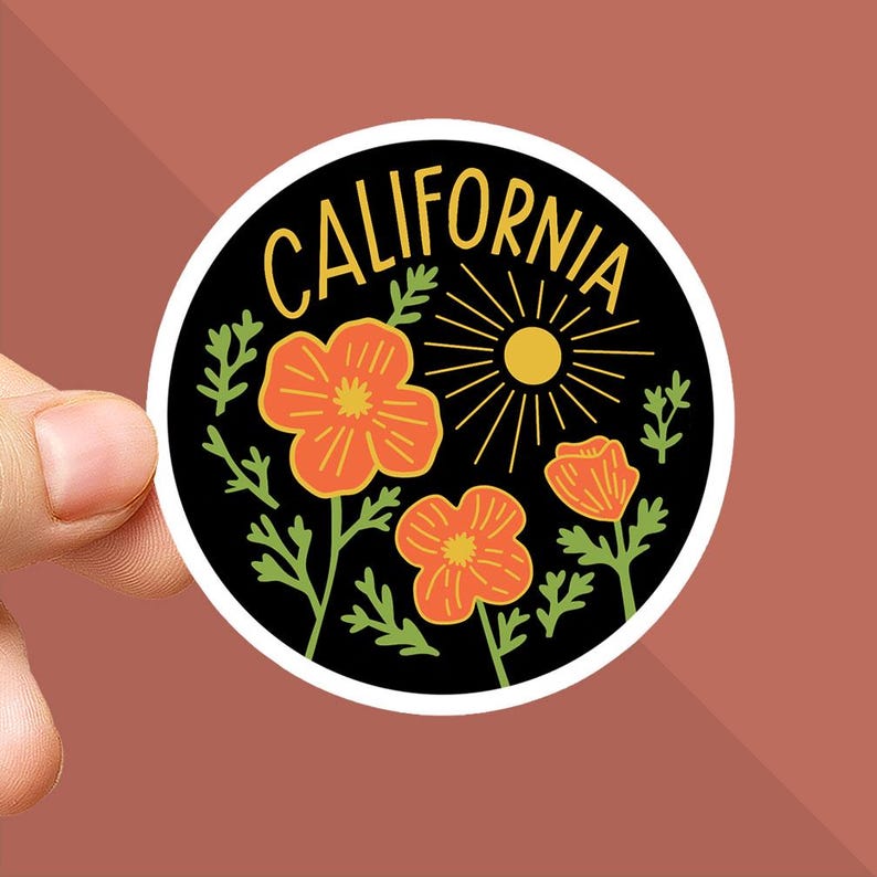 Peut inclure: Un autocollant rond avec un fond noir. Il pr&eacute;sente le mot "CALIFORNIA" en jaune, un soleil et des fleurs de pavot orange. L'autocollant a une bordure blanche et est tenu par une main.