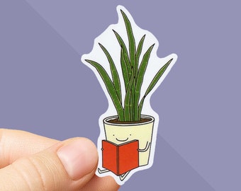 May include: A sticker featuring a cartoon illustration of a potted snake plant reading a book. The plant has long green leaves and is in a yellow pot with a smiling face. The book is red.