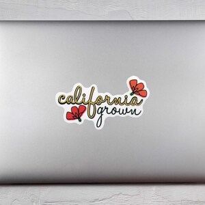 May include: A sticker with the words "california grown" in a cursive font, with a yellow outline and black shadow. Two red flowers with green stems are on the sticker. The sticker is on a silver laptop.