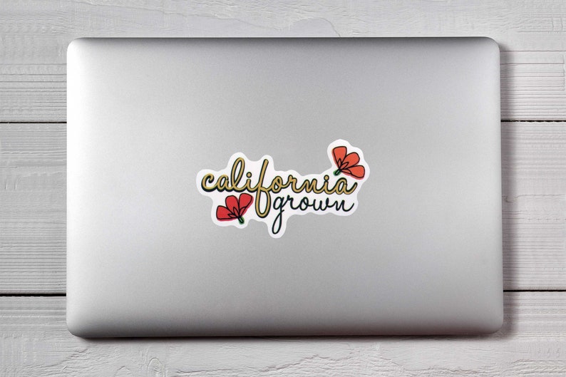 May include: A sticker with the words "california grown" in a cursive font, with a yellow outline and black shadow. Two red flowers with green stems are on the sticker. The sticker is on a silver laptop.