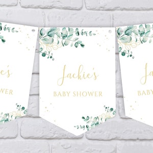 May include: Three white pennant banners with gold text and green watercolor foliage. The text on each banner reads "Jackie's Baby Shower".