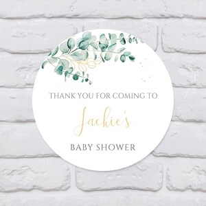 May include: Round white thank you tag with green eucalyptus leaves and gold accents. The text reads "Thank you for coming to Jackie's Baby Shower".