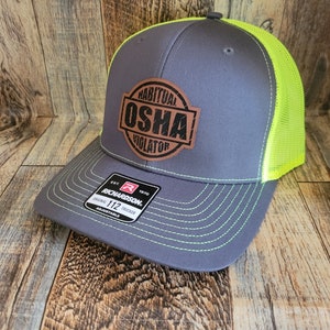 Könnte beinhalten: Eine graue und neongelbe Trucker-Kappe mit einem braunen Leder-Patch, auf dem "Habitual OSHA Violator" steht.