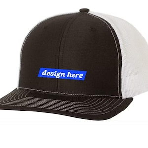 Peut inclure: Casquette de camionneur noire et blanche avec un patch rectangulaire bleu qui dit "design here" sur le devant.