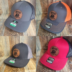 Puede incluir: Cuatro gorras de camionero con un parche de cuero marrón que dice "Técnico certificado de cinta adhesiva". Las gorras son de cuatro colores diferentes: gris, gris con malla naranja, negro con malla gris y rojo con malla negra.
