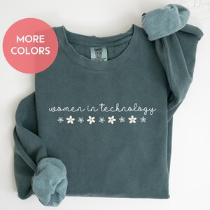May include: A teal blue sweatshirt with the text "women in technology" and a row of white daisies below.