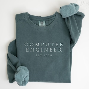May include: A teal blue sweatshirt with the text "COMPUTER ENGINEER EST. 2025" in white.