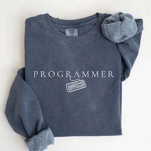 May include: A dark blue sweatshirt with the text "PROGRAMMER" and a white outline of a computer keyboard. The sweatshirt is folded in half and the sleeves are rolled up.