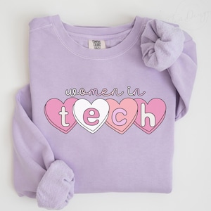 May include: A light purple sweatshirt with the words "women in tech" above four heart-shaped candies spelling out "tech". The candy hearts are pink and white with black outlines. The word "ORCHID" is printed in the bottom right corner.