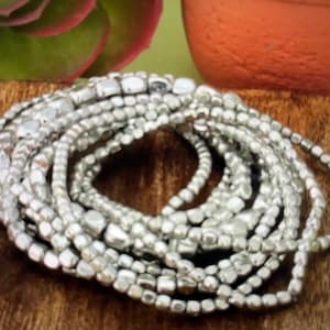 May include: A stack of silver-toned beaded bracelets. The beads are small and have a slightly irregular shape.