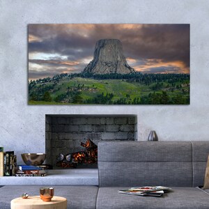 Könnte beinhalten: Ein Panoramafoto einer großen Felsformation, bekannt als Devils Tower, die aus einer grasbewachsenen Ebene aufragt. Der Himmel ist mit dramatischen Wolken gefüllt, die ein Gefühl von Größe und Ehrfurcht erzeugen.