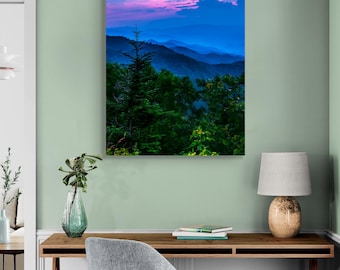 May include: A photograph of a mountain range at dusk with a pink and blue sky. The mountains are covered in trees and the sky is filled with clouds.