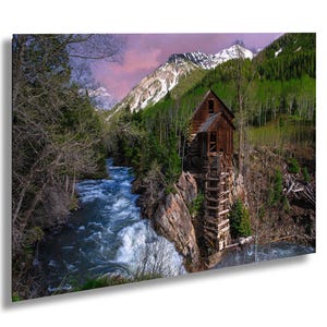 May include: A scenic landscape print featuring a wooden structure perched on a rocky cliffside next to a rushing river. The background includes snow-capped mountains, lush green trees, and a colorful sky.
