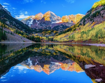 May include: A scenic view of Maroon Bells, a mountain range in Colorado, reflected in a still lake. The mountains are covered in snow and surrounded by colorful autumn foliage.