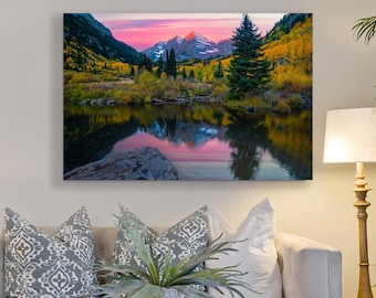 Puede incluir: Una fotografía de paisaje de un lago de montaña que refleja el cielo colorido de la puesta de sol. El lago está rodeado de árboles con follaje otoñal vibrante, incluyendo hojas amarillas, naranjas y rojas. Un árbol de hoja perenne alto se encuentra en el lado derecho de la imagen.