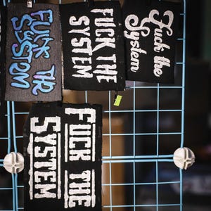 May include: A white ceramic mug with a black handle and the text "But First, Coffee" in a bold, black font. The mug is set against a blurred background, suggesting a cozy setting.
