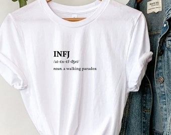 May include: White t-shirt with the text "INFJ /al-En-Ef-dget/ noun. a walking paradox" printed on the front.