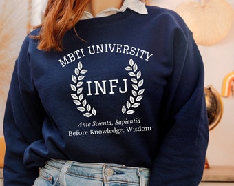 May include: A navy blue sweatshirt with the text "MBTI University" and a white wreath with the letters "INFJ" inside. The text "Ante Scientia, Sapientia" and "Before Knowledge, Wisdom" is printed below the wreath.