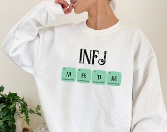 May include: White sweatshirt with a graphic of the letters "INFJ" and the chemical symbols for the elements "Ni", "Fe", "Ti", and "Se" in green squares.