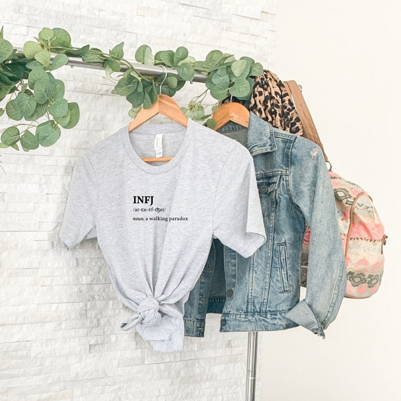 May include: A gray t-shirt with the text "INFJ /al-En-Ef-dget/ noun, a walking paradox" printed on the front.
