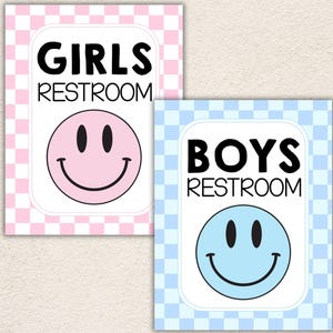 May include: Two rectangular signs with rounded corners. One sign has a pink and white checkered background with the text GIRLS RESTROOM and a pink smiley face. The other sign has a light blue and white checkered background with the text BOYS RESTROOM and a light blue smiley face.