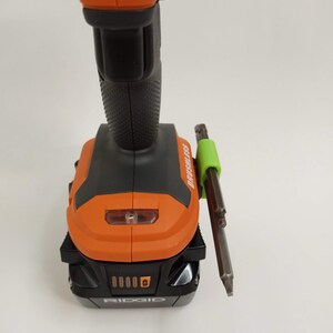 K&ouml;nnte beinhalten: Ein schwarzer und orangefarbener Akku-Bohrschrauber mit einem gr&uuml;nen magnetischen Bit-Halter an der Seite. Der Bohrschrauber hat einen Akku und der Text "RIDGID" ist auf dem Akku sichtbar.