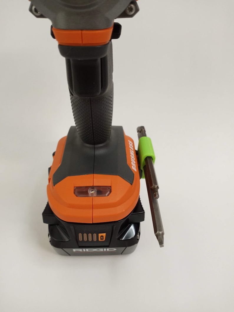 K&ouml;nnte beinhalten: Ein schwarzer und orangefarbener Akku-Bohrschrauber mit einem gr&uuml;nen magnetischen Bit-Halter an der Seite. Der Bohrschrauber hat einen Akku und der Text "RIDGID" ist auf dem Akku sichtbar.