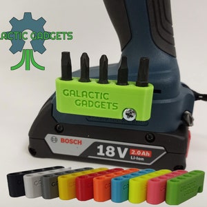 May include: A green 3D printed bit holder for a drill with the text "GALACTIC GADGETS" on it. The holder is attached to a black and blue drill battery. The image also shows a variety of colors for the bit holder.