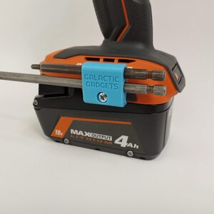 K&ouml;nnte beinhalten: Ein blauer 3D-gedruckter Werkzeughalter mit dem Text "GALACTIC GADGETS" befestigt an einem schwarzen und orangen Akkuschrauber-Akku. Der Halter h&auml;lt drei unterschiedlich gro&szlig;e Bohrer.