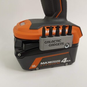May include: A black and orange power tool battery with a gray 3D printed bit holder that says "GALACTIC GADGETS". The battery is labeled "18v MAX OUTPUT LITHIUM 4Ah".