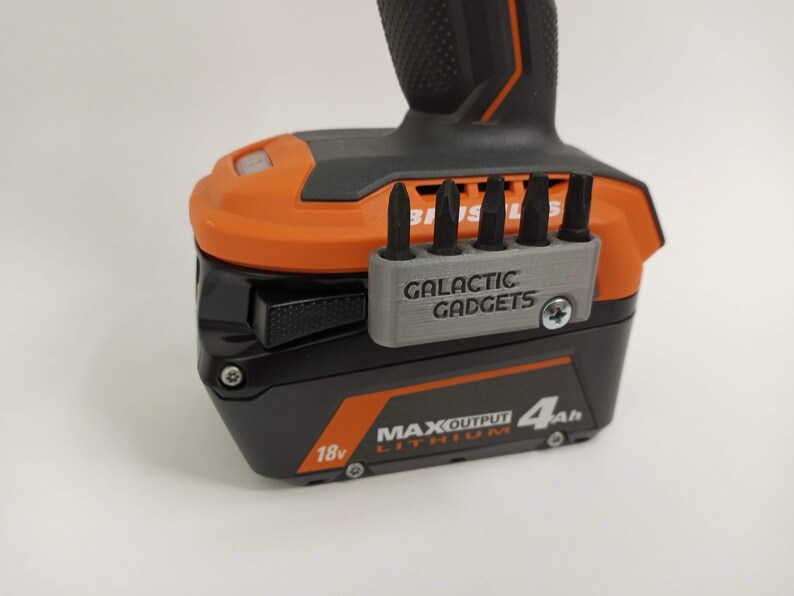 May include: A black and orange power tool battery with a gray 3D printed bit holder that says "GALACTIC GADGETS". The battery is labeled "18v MAX OUTPUT LITHIUM 4Ah".