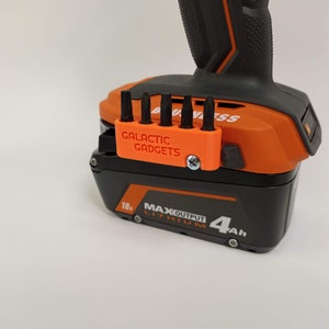 May include: Orange and black power tool battery with a 3D printed orange bit holder attached to the side. The bit holder has five slots for bits and says "GALACTIC GADGETS" on the front.
