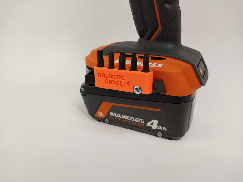 May include: Orange and black power tool battery with a 3D printed orange bit holder attached to the side. The bit holder has five slots for bits and says "GALACTIC GADGETS" on the front.