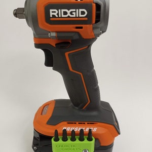 May include: An orange and black cordless impact wrench with a brushless motor. The wrench has a 18V battery with a 4Ah capacity. The battery is labeled "Max Output Lithium". The wrench is made by Ridgid.
