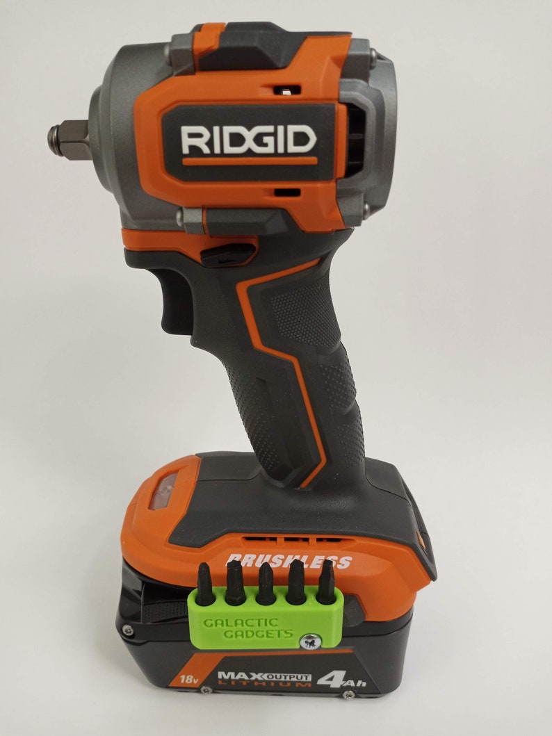 May include: An orange and black cordless impact wrench with a brushless motor. The wrench has a 18V battery with a 4Ah capacity. The battery is labeled "Max Output Lithium". The wrench is made by Ridgid.