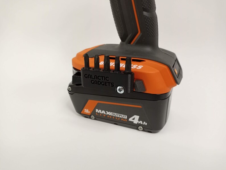 May include: A black 3D printed bit holder with the text "GALACTIC GADGETS" attached to an orange and black power tool battery. The battery is labeled "18v MAX OUTPUT LITHIUM 4Ah".