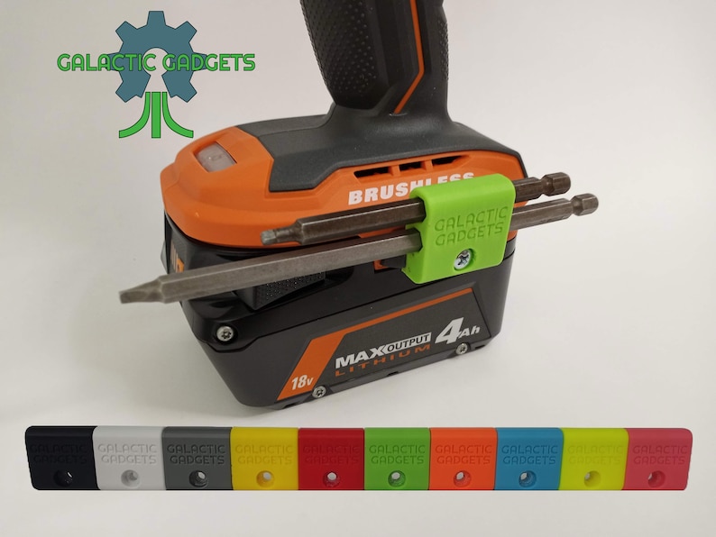 K&ouml;nnte beinhalten: Ein gr&uuml;ner 3D-gedruckter Werkzeughalter mit dem Text "GALACTIC GADGETS" befestigt an einem schwarzen und orangefarbenen Akku-Bohrschrauber. Der Halter h&auml;lt zwei Metallbohrer. Der Bohrschrauber hat einen 18-V-Akku mit dem Text "MAXOUTPUT 4Ah LITHIUM". Das Bild zeigt auch eine Reihe von 10 Werkzeughaltern in verschiedenen Farben: Schwarz, Wei&szlig;, Grau, Gelb, Rot, Gr&uuml;n, Orange, Blau, Hellgelb und Rot.