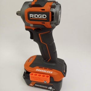 May include: An orange and black cordless impact wrench with a brushless motor and a 4Ah battery. The battery has a label that says "18V MAX OUTPUT LITHIUM ION 4Ah". The wrench has a black handle and a silver head. The wrench is made by RIDGID.