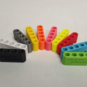 May include: A set of ten 3D printed multi-colored storage organizers with the text "Galactic Gadgets" printed on the bottom. The organizers are designed to hold small items like screws, nails, or beads.