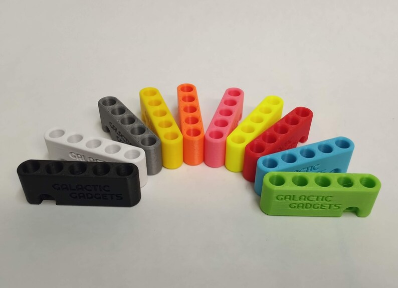 May include: A set of ten 3D printed multi-colored storage organizers with the text "Galactic Gadgets" printed on the bottom. The organizers are designed to hold small items like screws, nails, or beads.