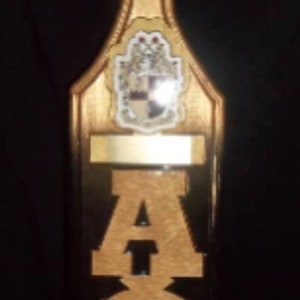 以下が含まれることがあります： 金色の仕上げが施された木製のパドルで、"ΑΦΑ"という文字が刻まれています。パドルには、盾と王冠がついた紋章があります。