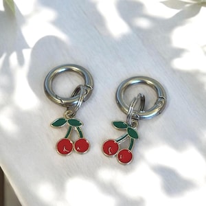 May include: Two silver keyrings with a red and green cherry charm. The charms are attached to silver rings with a spring clasp.