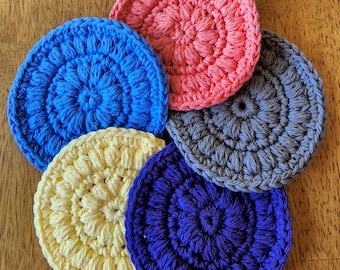 May include: Five crocheted cotton rounds in different colors: blue, yellow, purple, gray, and pink. The rounds are all about 4 inches in diameter and have a textured, raised pattern.